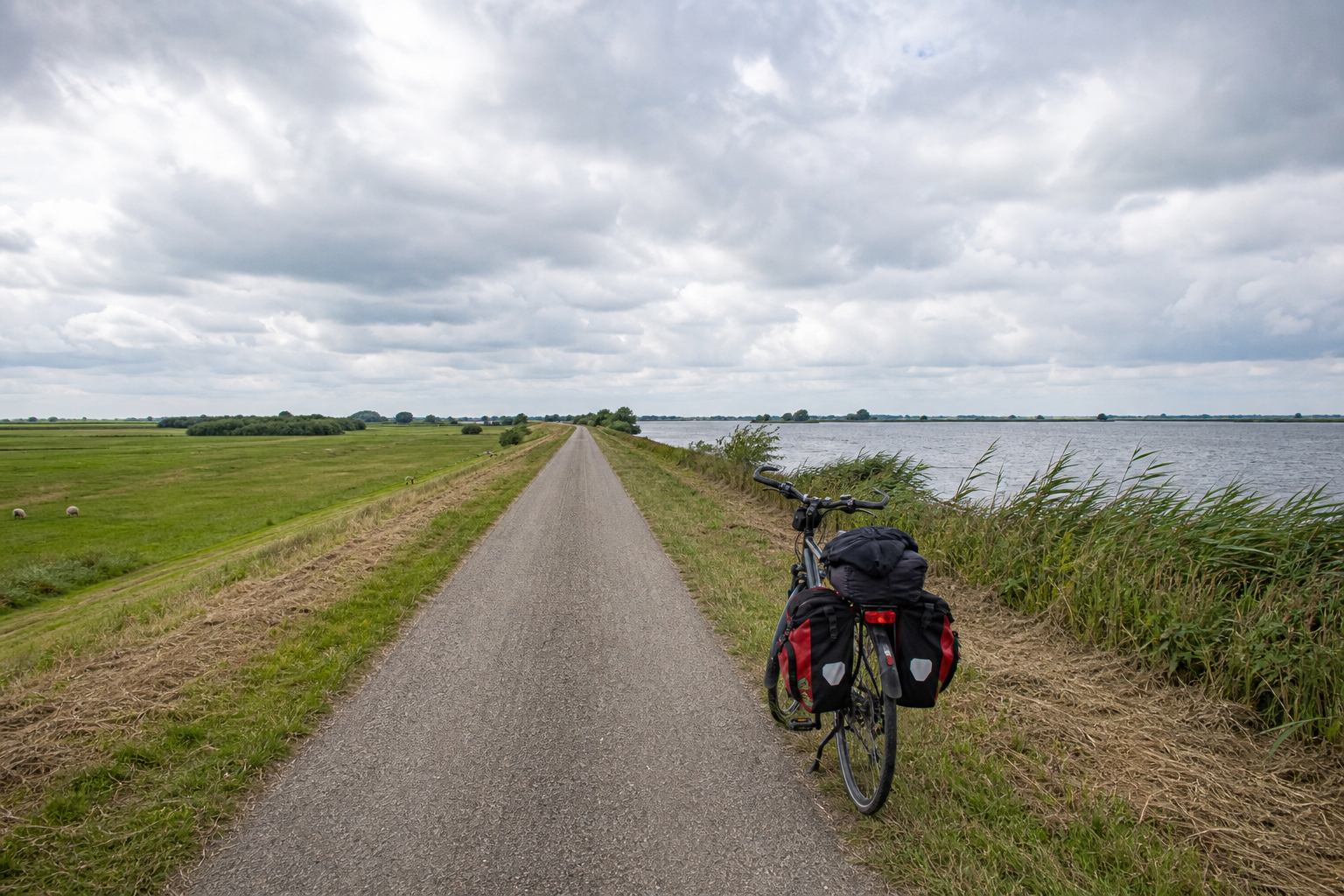 Long straight dike cycle track between a lake and flood meadows